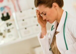 Female physician holding her head due to high, prolonged stress around preparing for her medical specialty board exams.